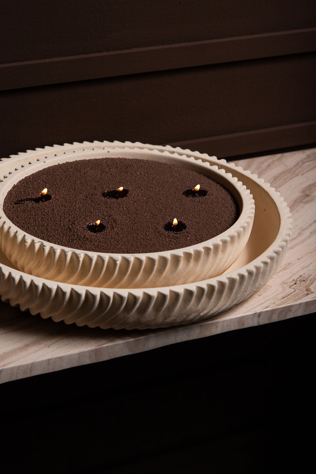 Beige Schalenkerze mit geriffeltem Rand, dunklem Wachs und fünf brennenden Dochten